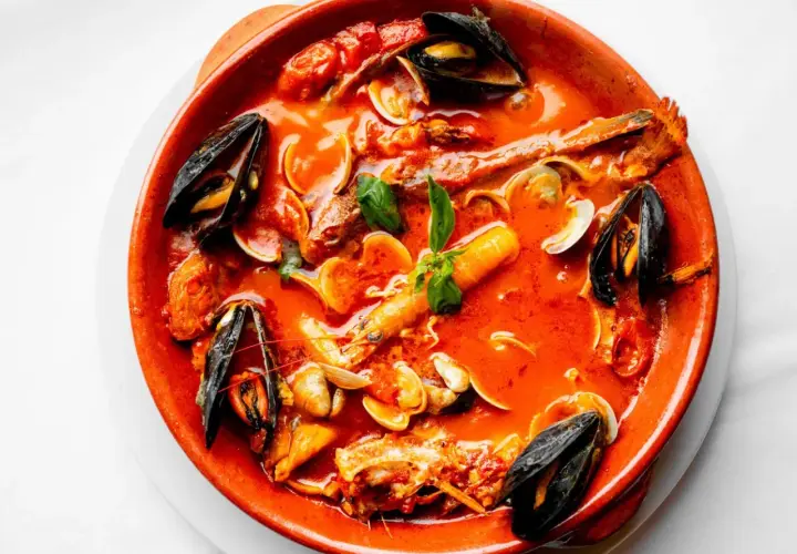 Un invitante brodetto di pesce in terracotta, ricco di cozze, vongole e gamberi, con un tocco di basilico fresco.