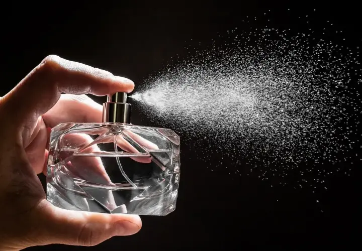 Dłoń trzyma szklaną butelkę, z której rozpyla się mgiełka. Czy to woda toaletowa czy perfumowana?