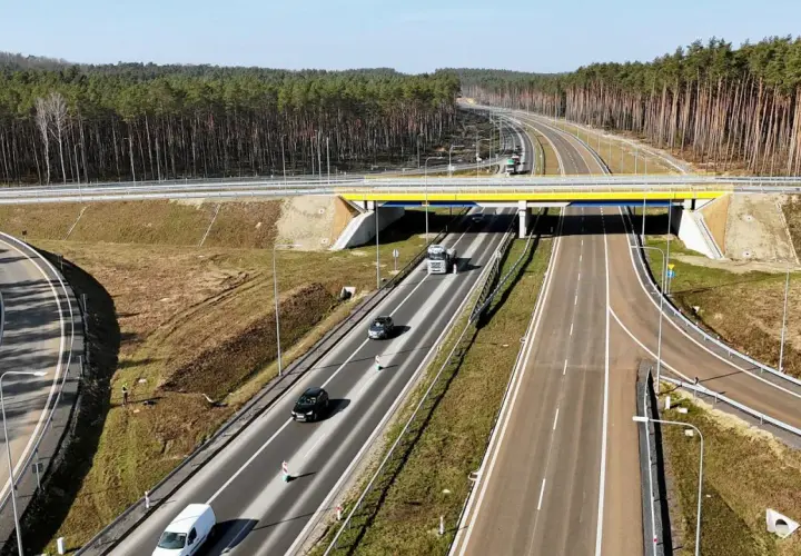 Droga ekspresowa z mostem, samochodami i ciężarówką. W tle las. Trudno ocenić, ile km na drodze ekspresowej.