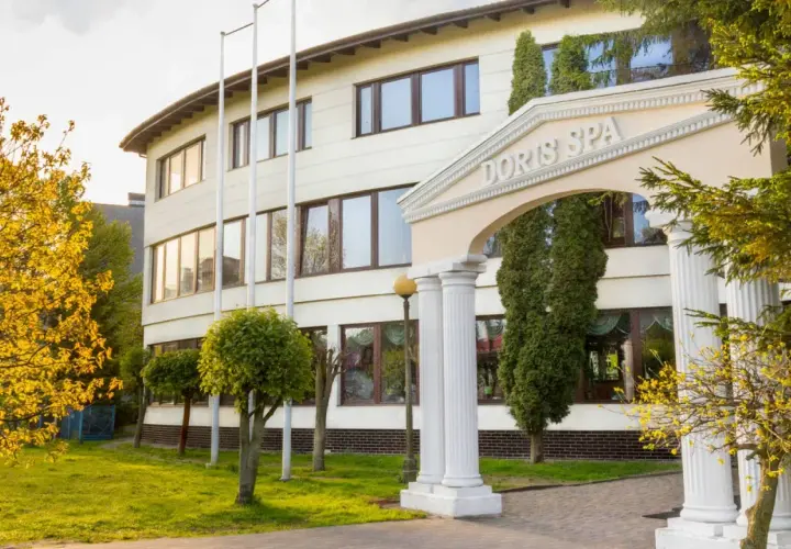 Elegancki budynek Doris Spa w Kołobrzegu z kolumnowym wejściem i kwitnącymi drzewami.