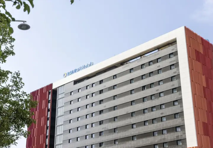 Edificio moderno con el logo "ILUNION Hotels" en la parte superior. Fachada gris con ventanas y detalles rojos.