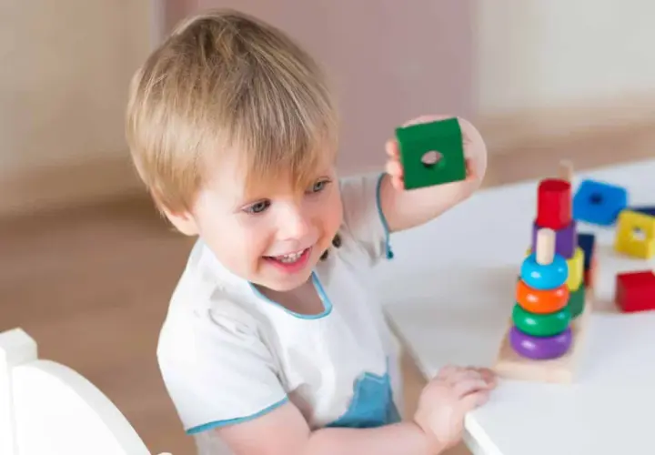 Bambino 3 anni sorridente gioca con blocchi colorati impilati.