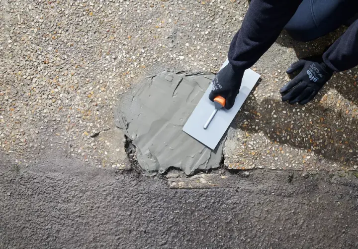 Rękawice i kielnia rozprowadzają zaprawę, wykonując naprawę betonu na zewnątrz.