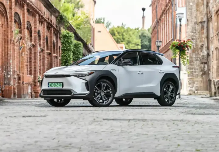Biały Toyota bz4x na brukowanej uliczce starego miasta, otoczony ceglanymi budynkami i zielenią.