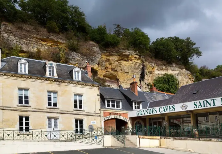 La maison Lacheteau, avec ses façades en pierre et ses toits d'ardoise, se dresse au pied d'une falaise rocheuse.