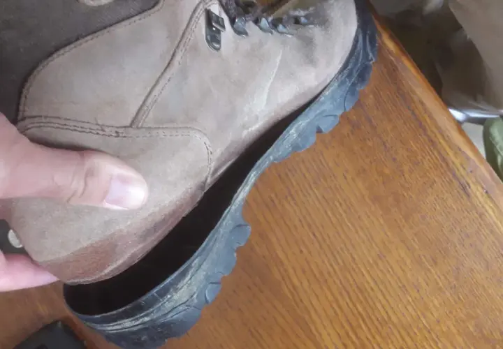 A hand holds a hiking boot where the sole is peeling off, revealing the inside of the shoe.