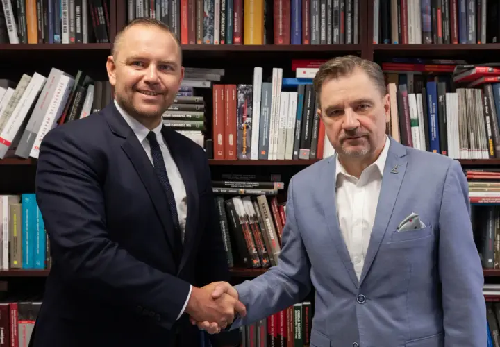 Dwóch mężczyzn w garniturach ściska sobie dłonie na tle regałów z książkami. Czy wybór Karola Nawrockiego na kandydata był konsultowany z Andrzejem Dudą?