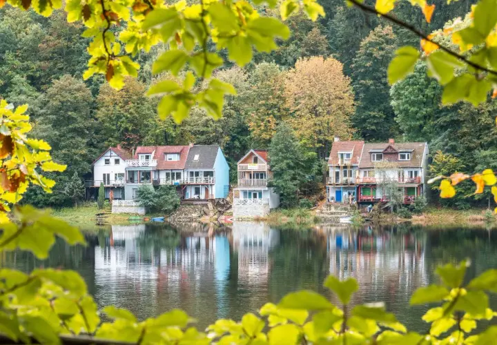 Domki nad jeziorem w jesiennej scenerii, odbijające się w wodzie.