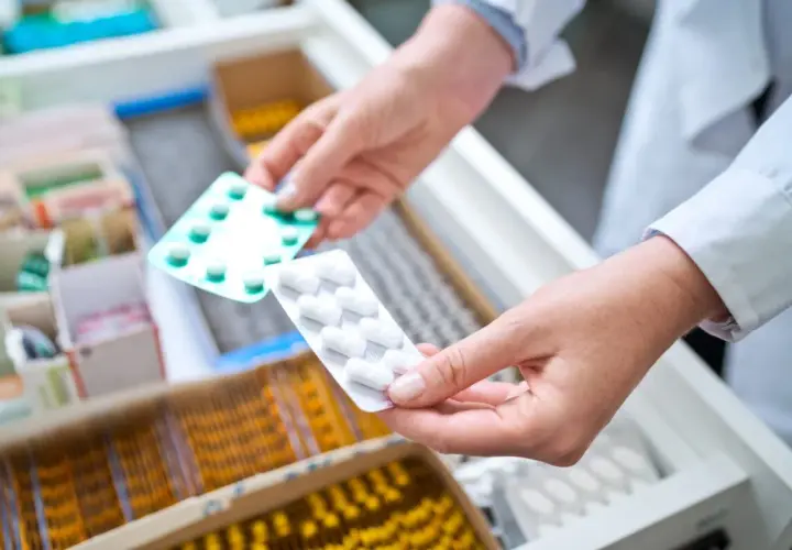Farmaceuta wybiera opakowanie tabletek, być może zawierających doloxib, z szuflady aptecznej.