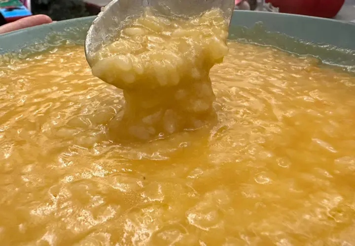 Un mestolo solleva una porzione cremosa di riso e patate, un comfort food caldo e invitante.