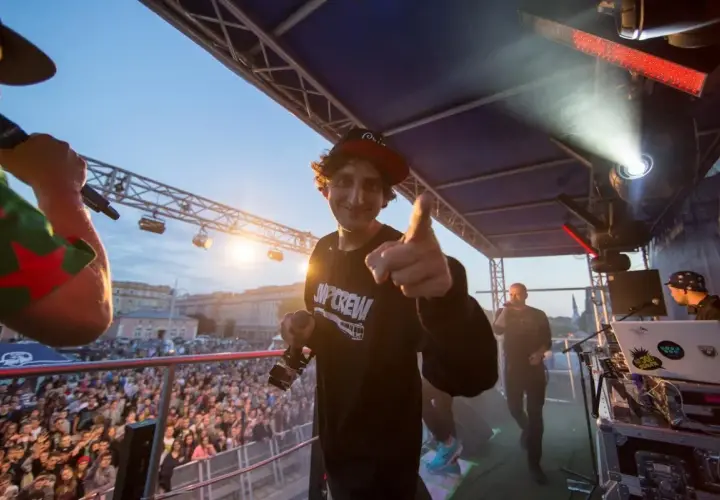 Kosi z JWP Crew w wieku około 30 lat, na scenie z mikrofonem, wskazuje palcem na widownię.