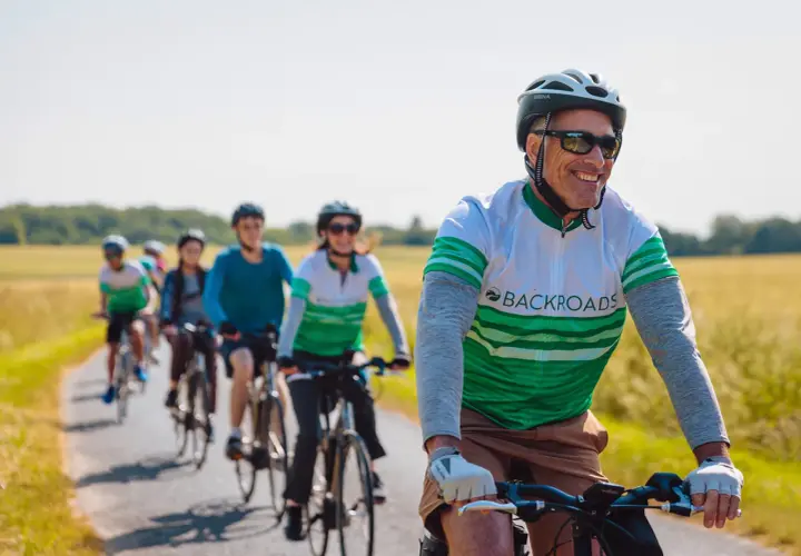 A group enjoys family cycling holidays on a sunny day, riding bikes down a paved path through golden fields.