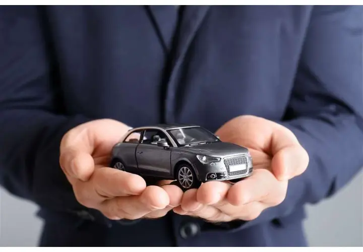 Mani che sorreggono un modellino d'auto grigio. Non dimenticare la tua assicurazione scaduta 15 giorni fa!