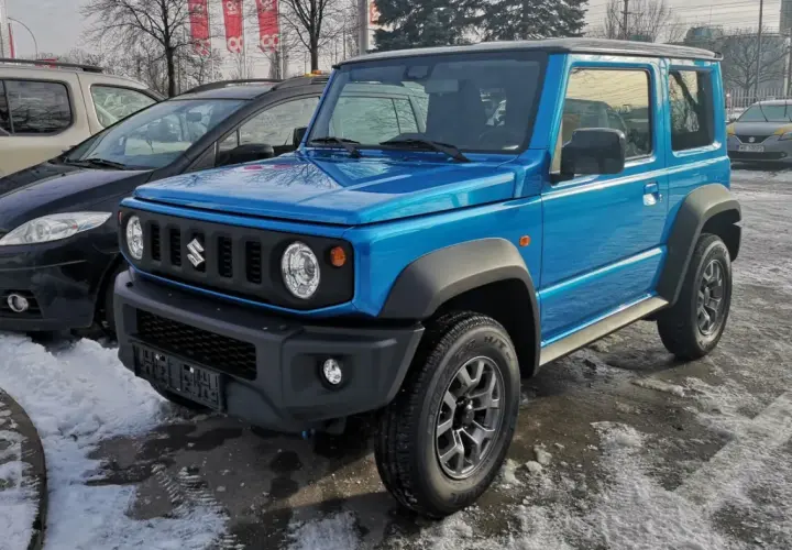 Niebieski Suzuki Jimny 2026 gotowy na zimowe przygody, zaparkowany na śniegu obok innych samochodów.