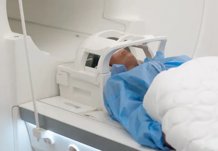 Pacjent leży w aparacie do rezonansu głowy, otoczony białym sprzętem medycznym.