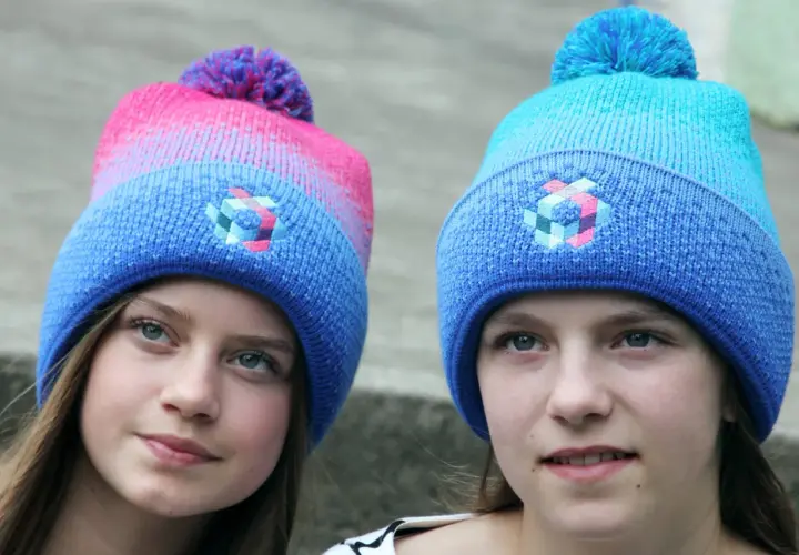 Zwei Mädchen mit bunten Bommelmützen in Blau und Pink.
