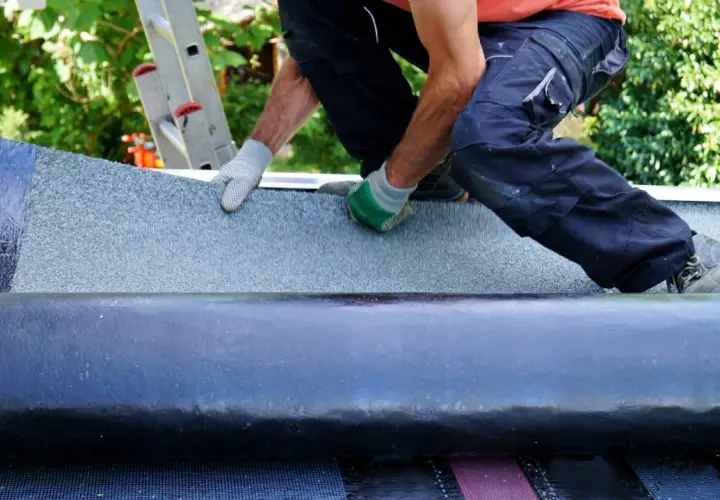 Handwerker klebt Dachpappe. Mit Handschuhen wird die Bitumenbahn sorgfältig ausgerollt und befestigt, um das Dach wetterfest zu machen.