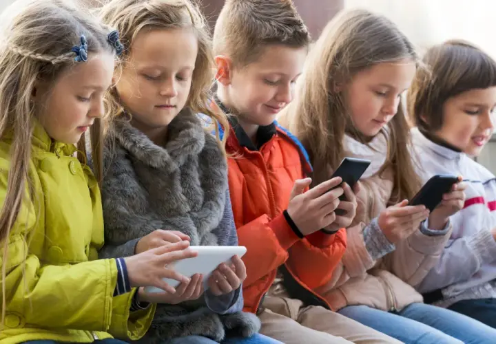 Dzieci skupione na ekranach telefonów i tabletu, szukają najlepszych gier dla 4 latka na telefon.
