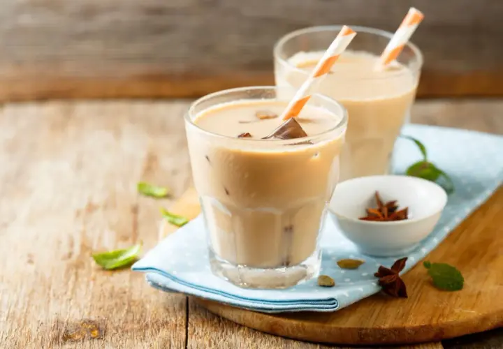 Dwa orzeźwiające **chai latte** z kostkami lodu i słomkami, ozdobione listkami mięty i przyprawami.