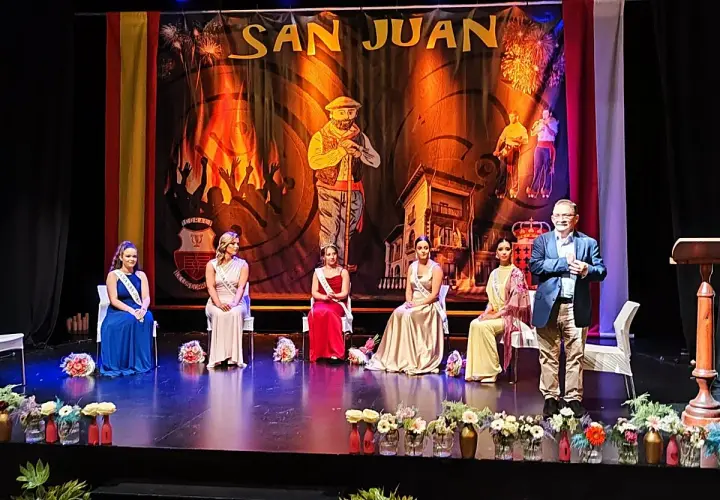En el teatro Los Corrales de Buelna, cinco damas de honor y un presentador esperan en el escenario bajo un telón de San Juan.