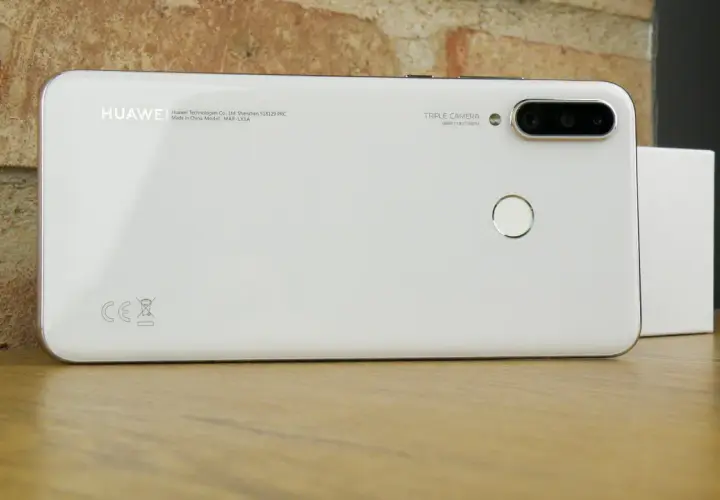 Biały smartfon Huawei MAR-LX1A z potrójnym aparatem i czytnikiem linii papilarnych na drewnianym blacie.
