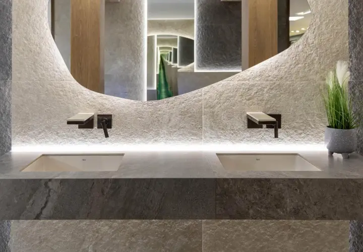 Nowoczesna łazienka z dwoma umywalkami, kamiennymi płytkami i rośliną, idealnie oddająca zasady biophilic design.