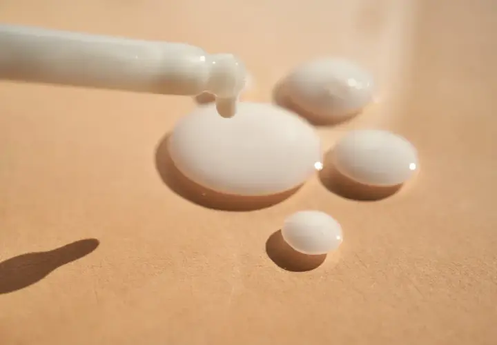 Ein weißes Serum tropft aus einem Applikator auf eine beige Oberfläche. Das ist Panthenol, ein Wirkstoff für Haut und Haar.