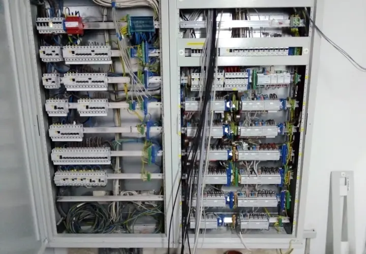Otwarta skrzynka elektryczna z licznymi przewodami i bezpiecznikami.