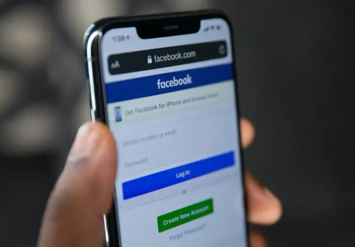 Dłoń trzyma smartfon z ekranem logowania Facebooka. Widoczny formularz do wpisania numeru telefonu/emaila i hasła, przycisk "Log In" oraz opcja "Forgot Password" - pomoc w sytuacji, jak odzyskać konto na FB.