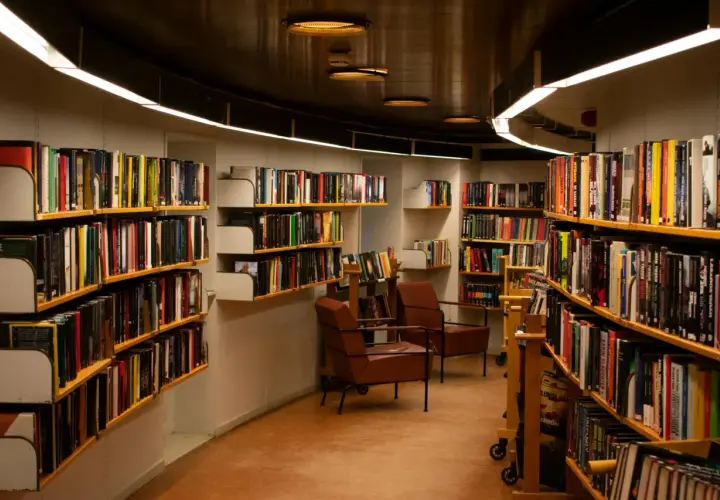 Wnętrze biblioteki z regałami pełnymi książek. Wygodne fotele zapraszają do lektury, a każdy tom czeka na swojego bibliotekarza.