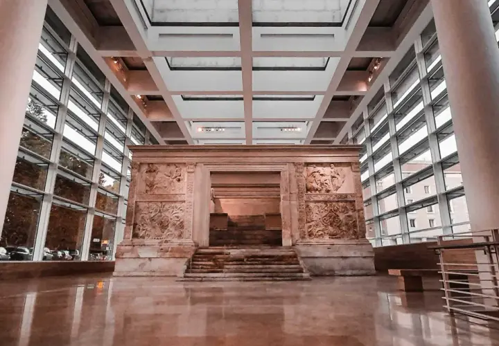 L'Ara Pacis, un altare monumentale con rilievi antichi, si erge maestoso in un moderno spazio espositivo con ampie vetrate.