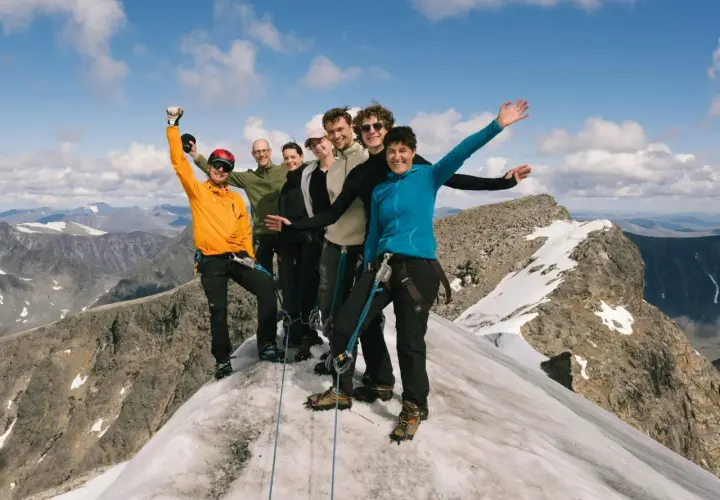 Glada vandrare på en snöig bergstopp, med Kebnekaise Silverfallet i bakgrunden.