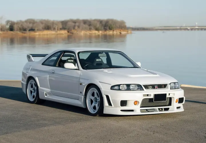 Białe r33 GT-R z siedzeniami Nismo stoi nad jeziorem.
