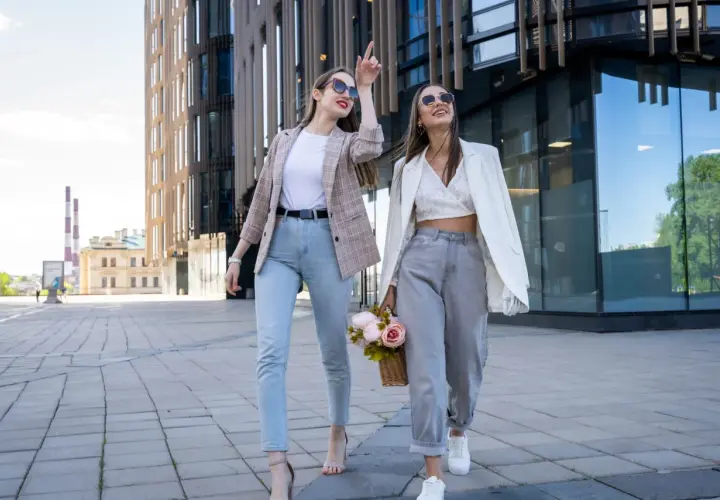 Dwie kobiety w modnych stylizacjach spacerują przed nowoczesnym budynkiem. Ich ubiór sugeruje, że to polskie marki znane na świecie.