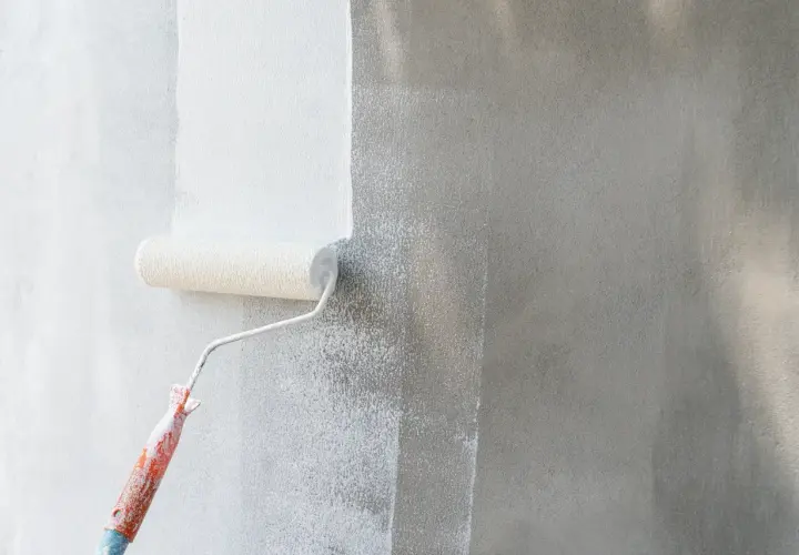 Rodillo aplicando imprimación blanca sobre pared gris. La imprimación prepara la superficie para la pintura.