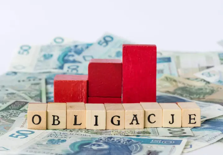 Drewniane klocki z napisem "OBLIGACJE" na tle polskich banknotów. Czerwone klocki tworzą wykres wzrostu.