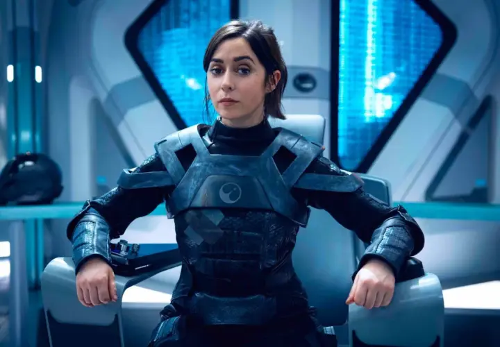 Une femme en armure futuriste, assise dans un cockpit, pourrait être un personnage de Black Mirror saison 7.