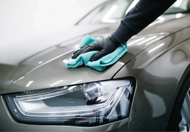 Mano guantata lucida la carrozzeria di un'auto con un panno azzurro. Il dettaglio mostra la cura per il costo lucidatura auto.