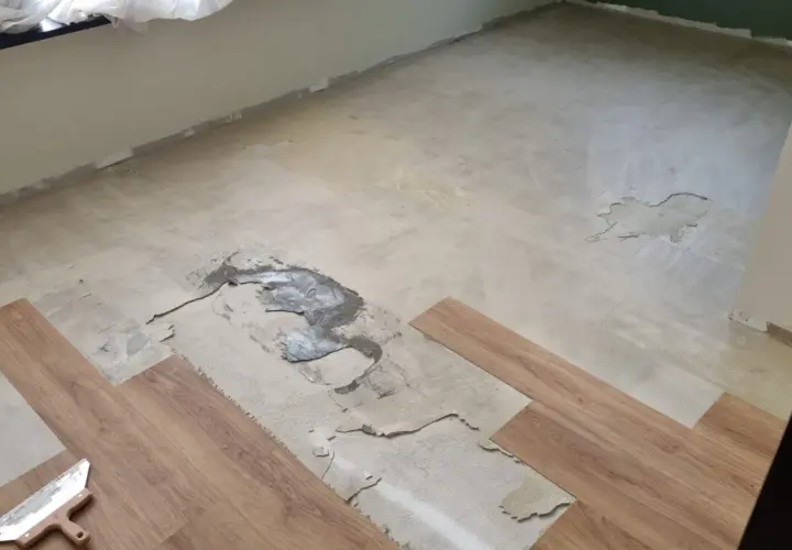 Il pavimento in PVC si solleva in più punti, mostrando il sottofondo danneggiato. Si vedono nuove doghe di legno pronte per la posa.