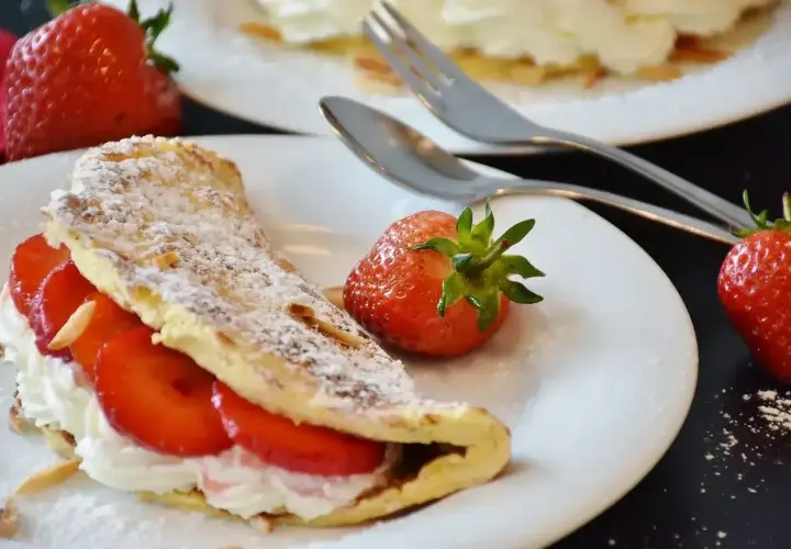 Słodki omlet z bitą śmietaną i truskawkami, posypany cukrem pudrem. Idealny przepis na omlet na deser.