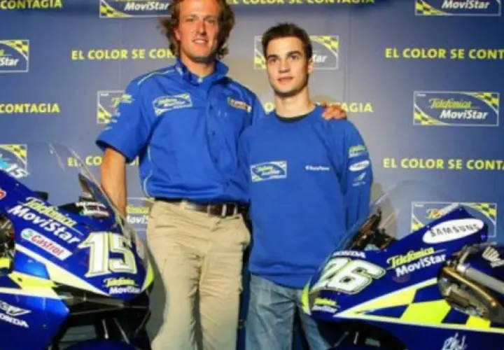 Sete Gibernau, con su edad, posa junto a un joven piloto, ambos con ropa de equipo azul, frente a motocicletas de competición.