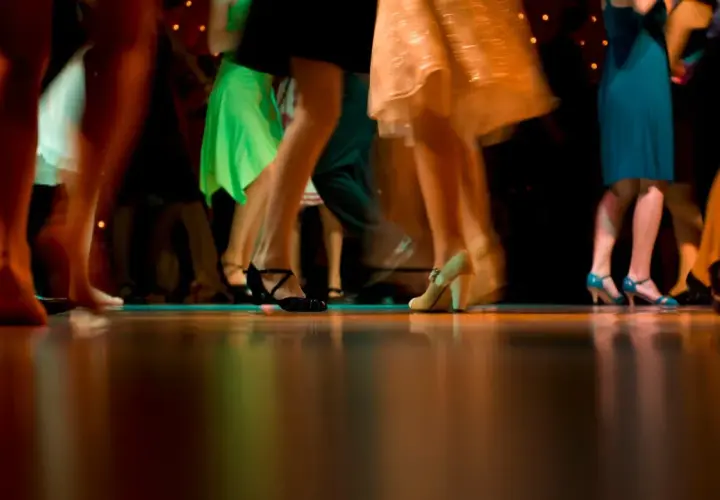 Nogi w ruchu, błyszczące sukienki i eleganckie buty. Wszyscy tańczą, tworząc dynamiczny obraz, jakby to był belgijka taniec.