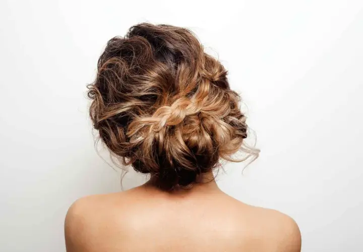 Un elegante recogido alto con pelo rizado y un detalle de trenza rubia.