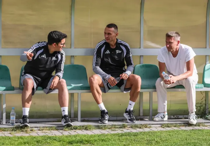 Trzech mężczyzn siedzi na ławce. Dwóch w strojach sportowych, jeden w białej koszulce. To trener Lechii Gdańsk i jego współpracownicy.