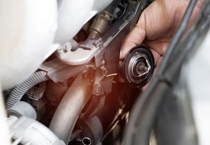 Mano che rimuove la valvola termostatica, forse perché non chiude bene e causa problemi al motore.