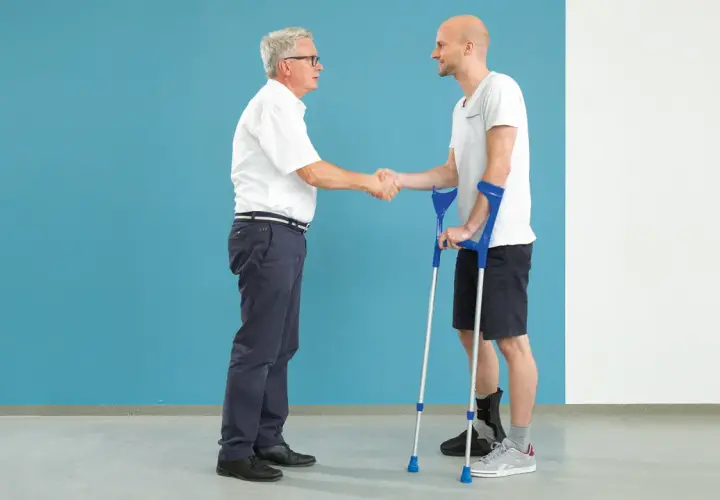 Arzt schüttelt Hand eines Patienten mit Krücken und Orthese am Fuß nach einer Calcaneusfraktur.