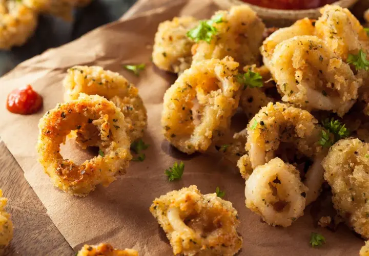 Anelli dorati e croccanti di calamari gratinati al forno, guarniti con prezzemolo fresco e accompagnati da una salsa rossa.