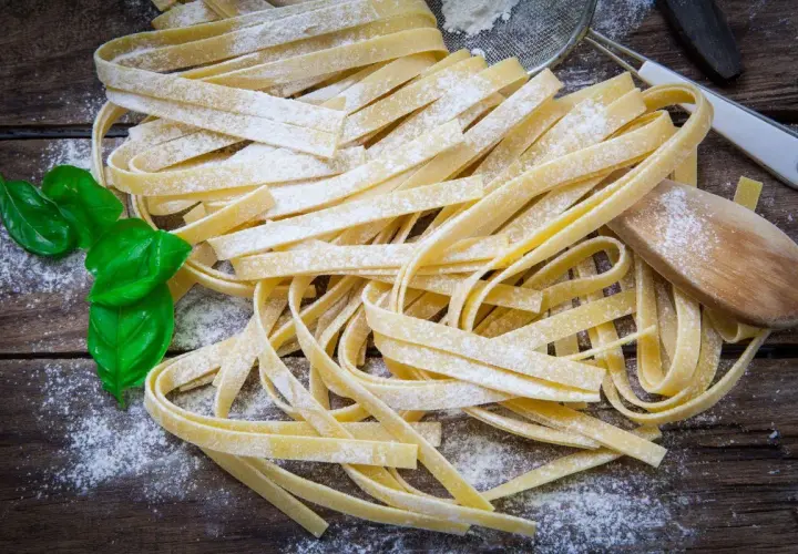 Świeży makaron tagliatelle, posypany mąką, z listkami bazylii. Idealny jako alternatywa, czym zastąpić makaron pszenny.