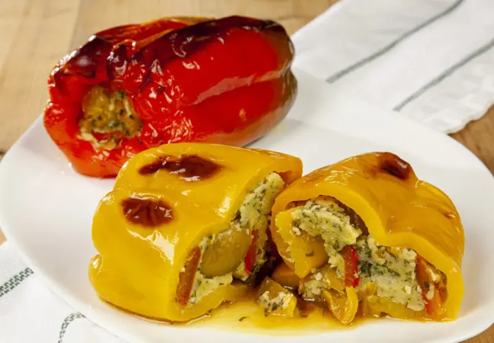 Peperoni ripieni senza carne, un piatto colorato e saporito. Un peperone rosso intero e uno giallo tagliato a metà, entrambi farciti con un ripieno gustoso.