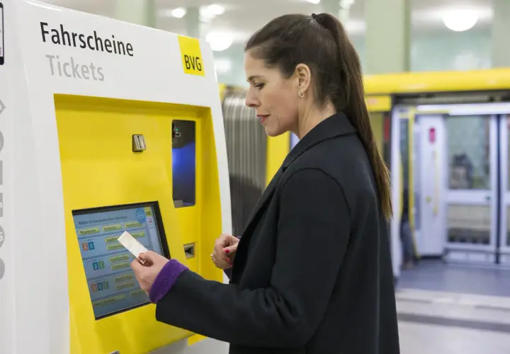 Frau kauft am Automaten ein Ticket. Die Bedeutung von SPNV (Schienenpersonennahverkehr) wird hier durch den Kauf eines Fahrscheins für die Fahrt mit Bus oder Bahn deutlich.